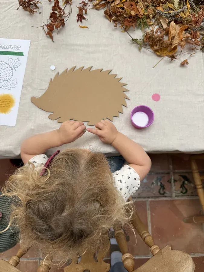 A child gluing a cardboard hedgehog shape