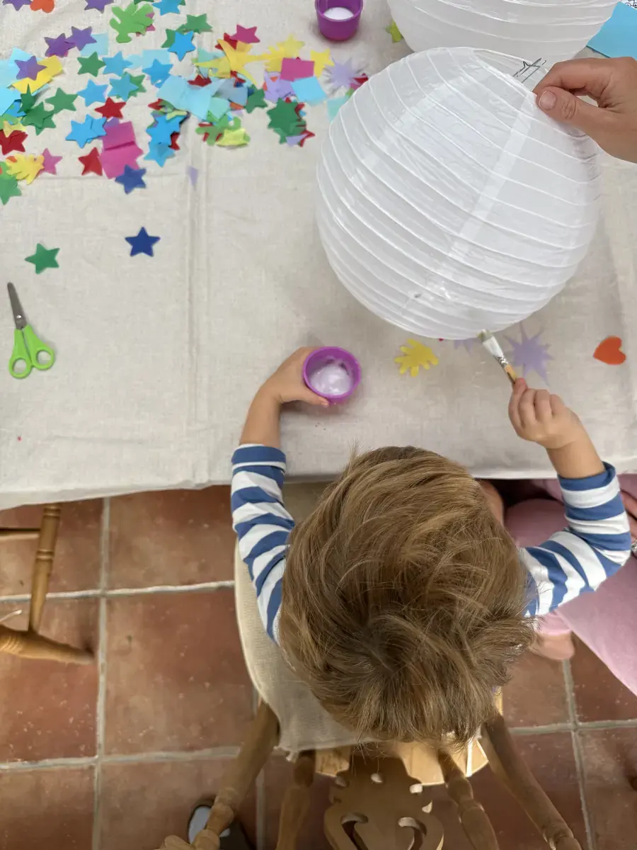 A child with a pot of glue decorating a paper lantern