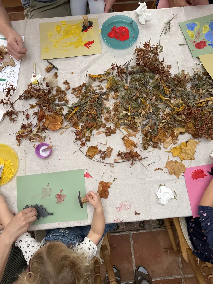 A child printing onto green paper beside a pile of autumn leaves