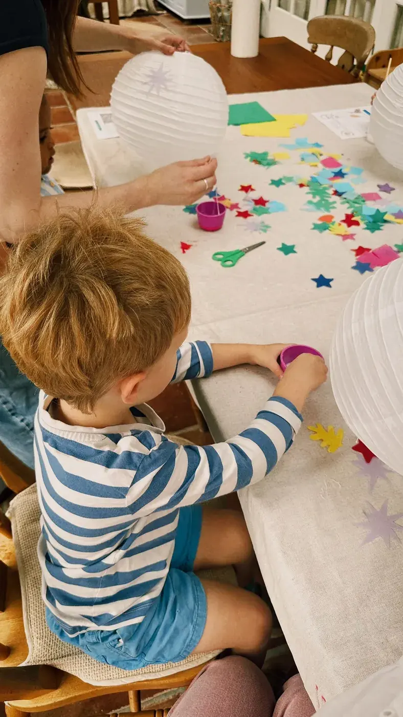 A child reaching for paper stars beside a paper lantern