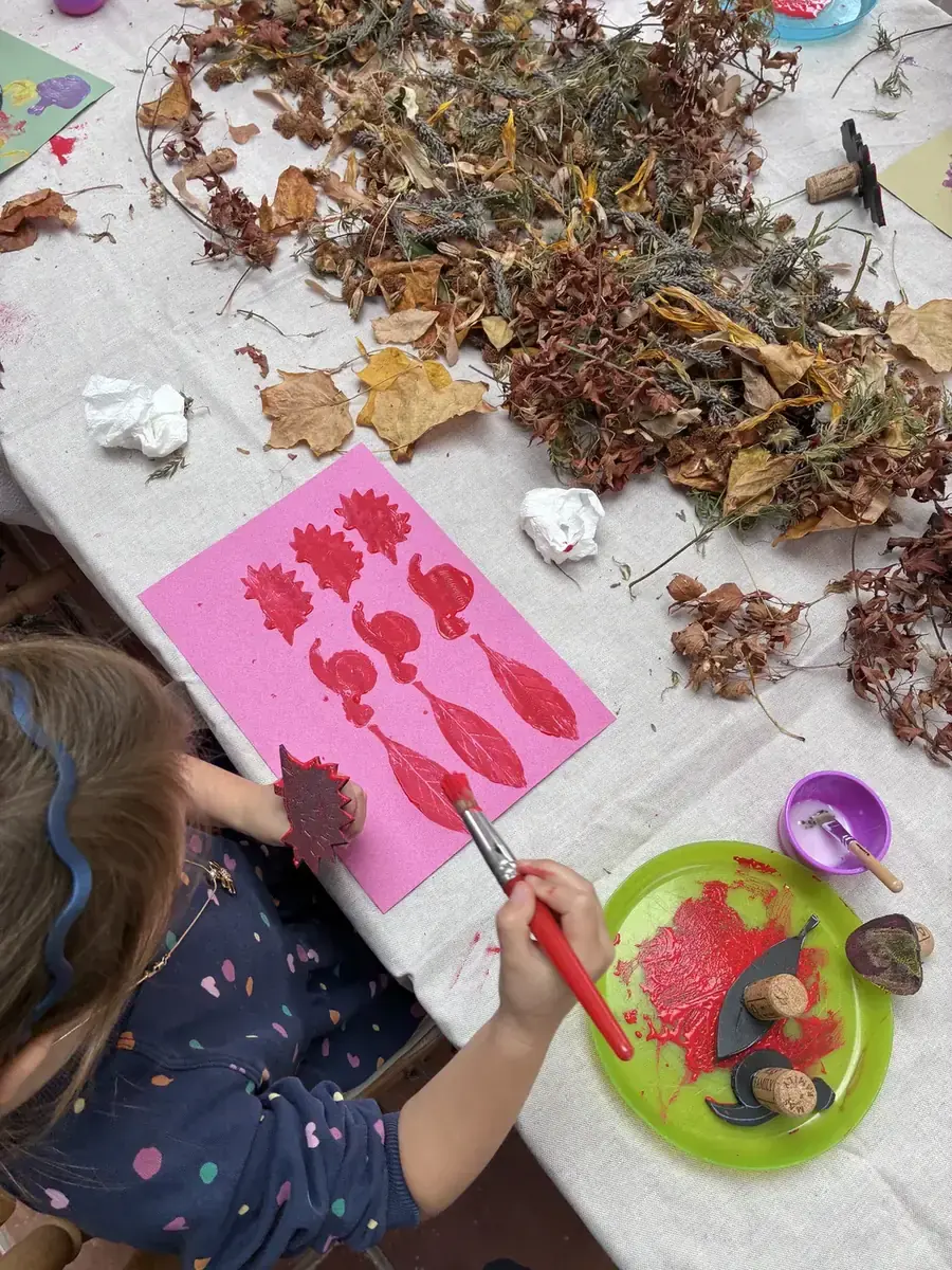 A child printing red leaf shapes onto pink paper